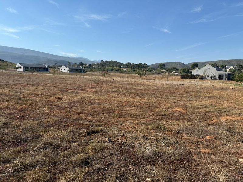 A wide-angle view of a vacant residential plot featuring natural landscape and surrounding mountain scenery.