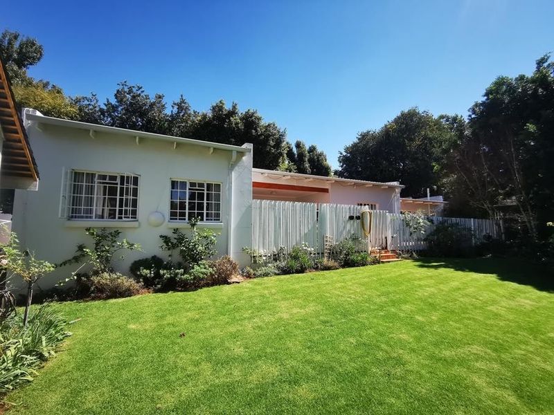 Rear view of the property featuring a well-maintained lawn, a white timber picket fence, and a covered patio area.