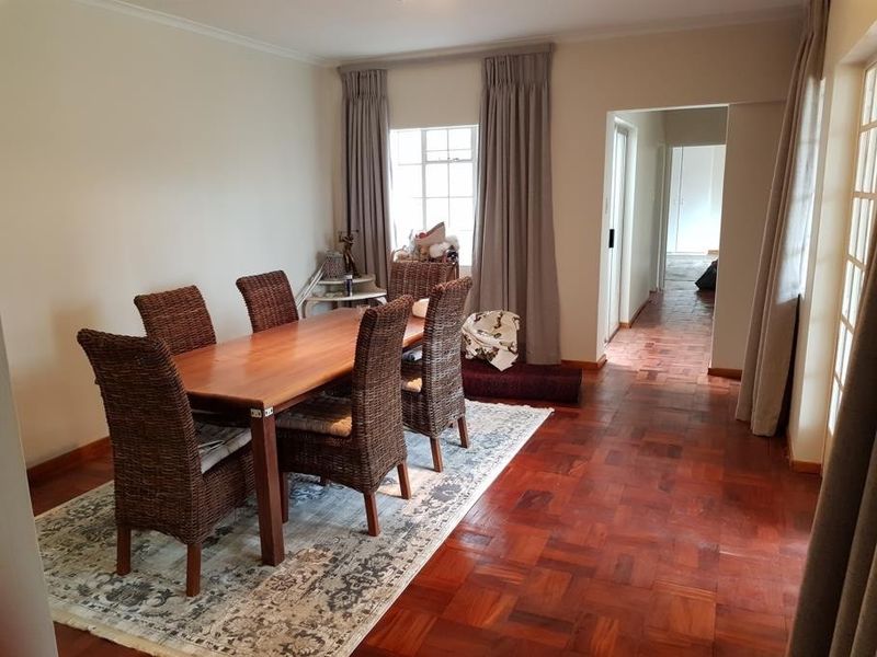 A dining room featuring classic parquet flooring, neutral walls, and natural light through timber-framed windows, leading into a hallway.
