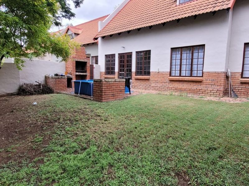 Rear view of the townhouse featuring a private garden, brick built-in braai area, and classic terracotta roof tiles.