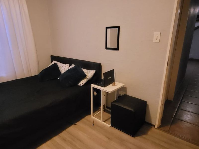 A standard bedroom featuring laminate flooring and a window, with a view leading into the hallway of the townhouse.