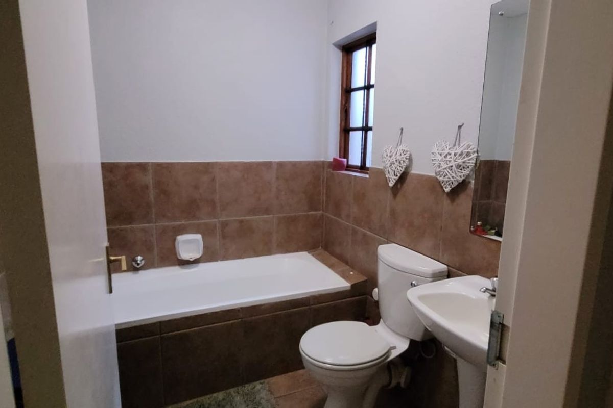 A functional bathroom featuring a bathtub with tiled surround, a pedestal basin, and a toilet, finished with neutral wall tiles.