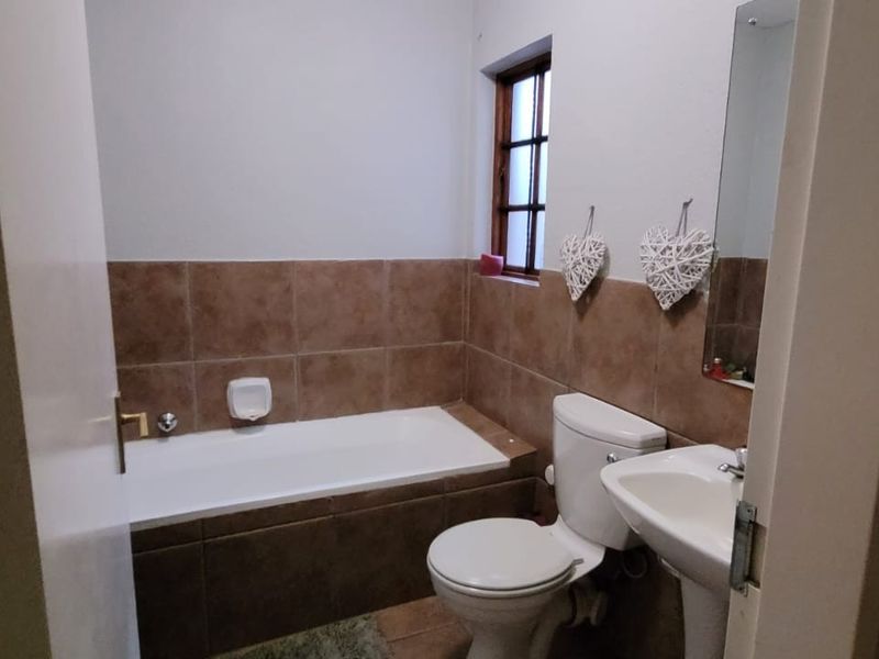 A functional bathroom featuring a bathtub with tiled surround, a pedestal basin, and a toilet, finished with neutral wall tiles.
