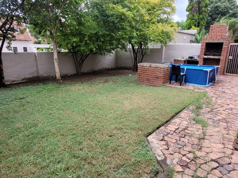 Private rear garden featuring a paved patio area, built-in brick braai, and a lawn enclosed by high boundary walls.