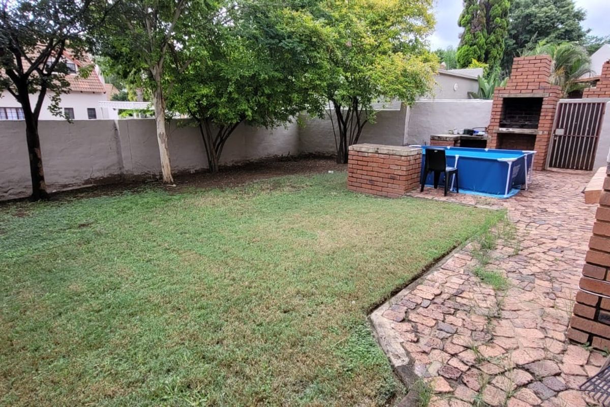 Private rear garden featuring a paved patio area, built-in brick braai, and a lawn enclosed by high boundary walls.