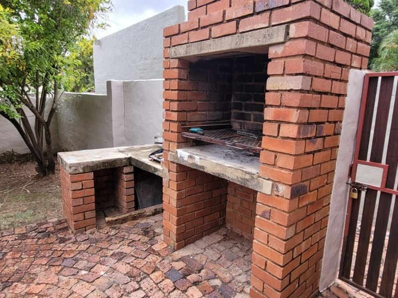 Outdoor patio area featuring a built-in brick braai, concrete prep counter, and brick paving, enclosed by a boundary wall and metal gate.