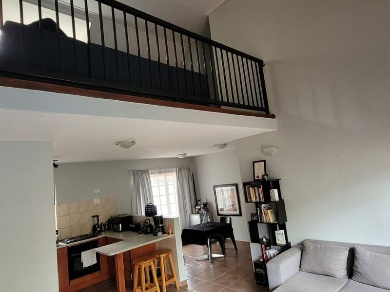 Open-plan living area featuring a mezzanine level, tiled flooring, and a functional kitchen with built-in cabinetry and breakfast counter.