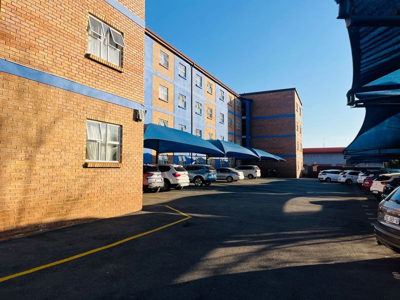 Exterior view of an apartment complex featuring a brick facade, asphalt parking area, and covered shade cloth parking bays.