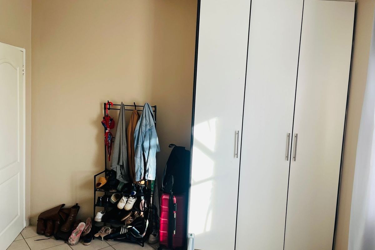 A bedroom featuring a white built-in wardrobe with modern handles and neutral tiled flooring.