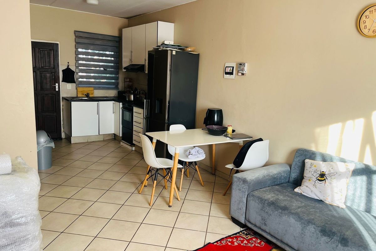 Open-plan living area featuring a compact kitchen with built-in cabinetry, oven, and extractor fan, seamlessly flowing into the dining and lounge space.
