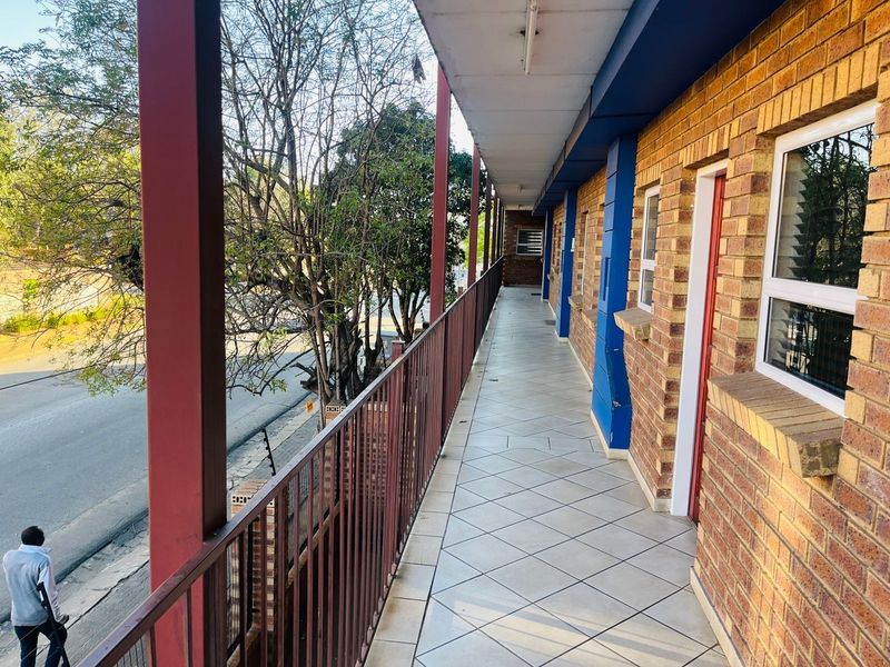 An exterior apartment balcony featuring tiled flooring, brick walls, and metal balustrades overlooking the street.