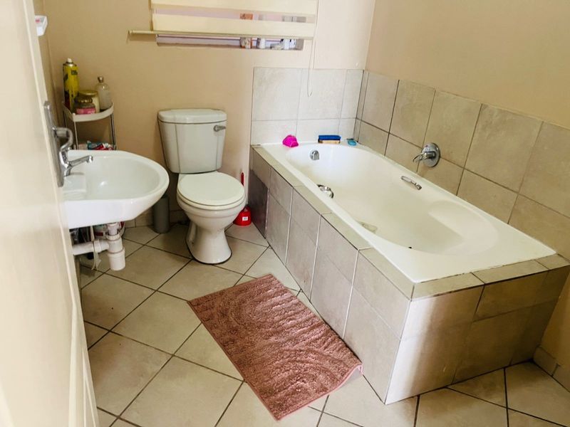 A functional bathroom featuring a built-in bathtub with tiled surround, a standard toilet, and a wall-mounted basin with ceramic floor tiling.