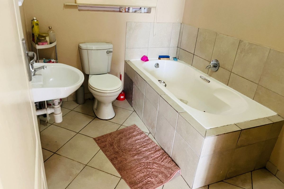 A functional bathroom featuring a built-in bathtub with tiled surround, a standard toilet, and a wall-mounted basin with ceramic floor tiling.