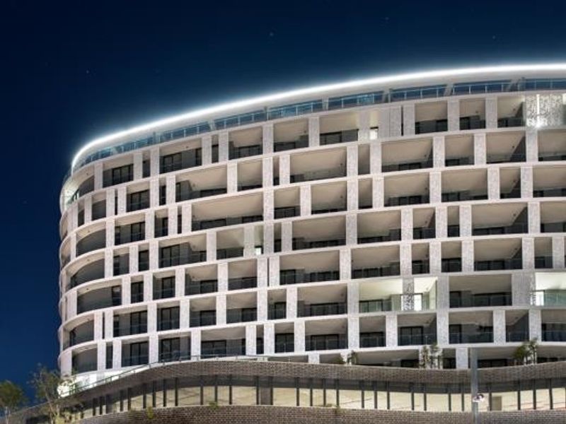 Night view of the modern Ellipse Waterfall apartment complex featuring a distinctive curved facade, integrated architectural lighting, and structured balcony design.