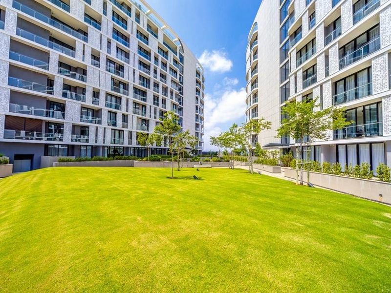 A well-maintained communal garden area situated between modern apartment blocks featuring glass balconies and decorative architectural facade detailing.