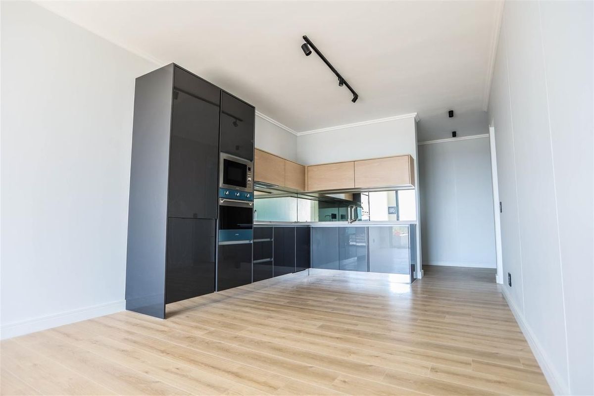 Modern kitchen featuring sleek dark grey and light wood cabinetry, integrated appliances, a mirror splashback, and contemporary track lighting.