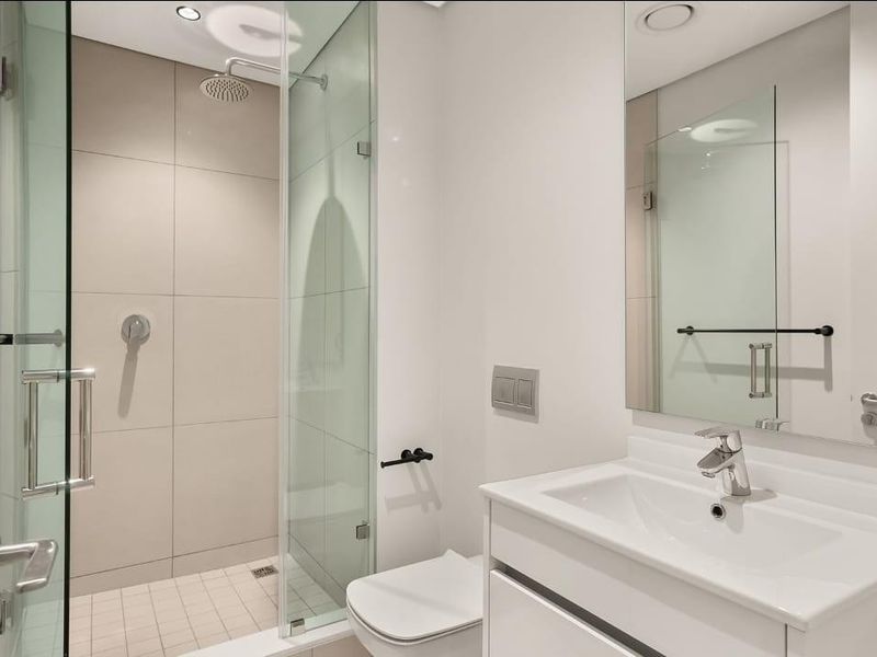 Modern bathroom featuring a glass-enclosed shower, wall-mounted toilet, and a sleek vanity with a large mirror, finished with neutral tiling.