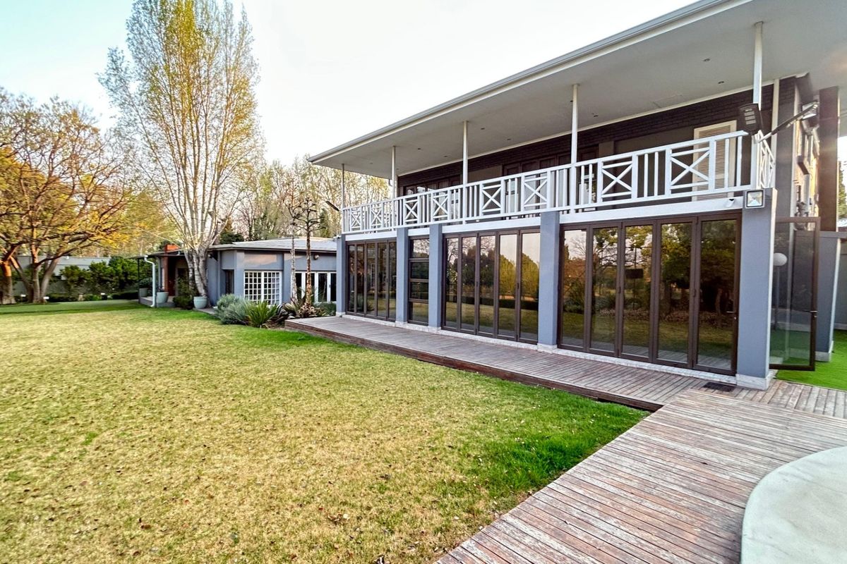 Spacious rear exterior featuring a large lawn, timber decking, and a covered patio with extensive folding glass doors leading to the upper balcony.