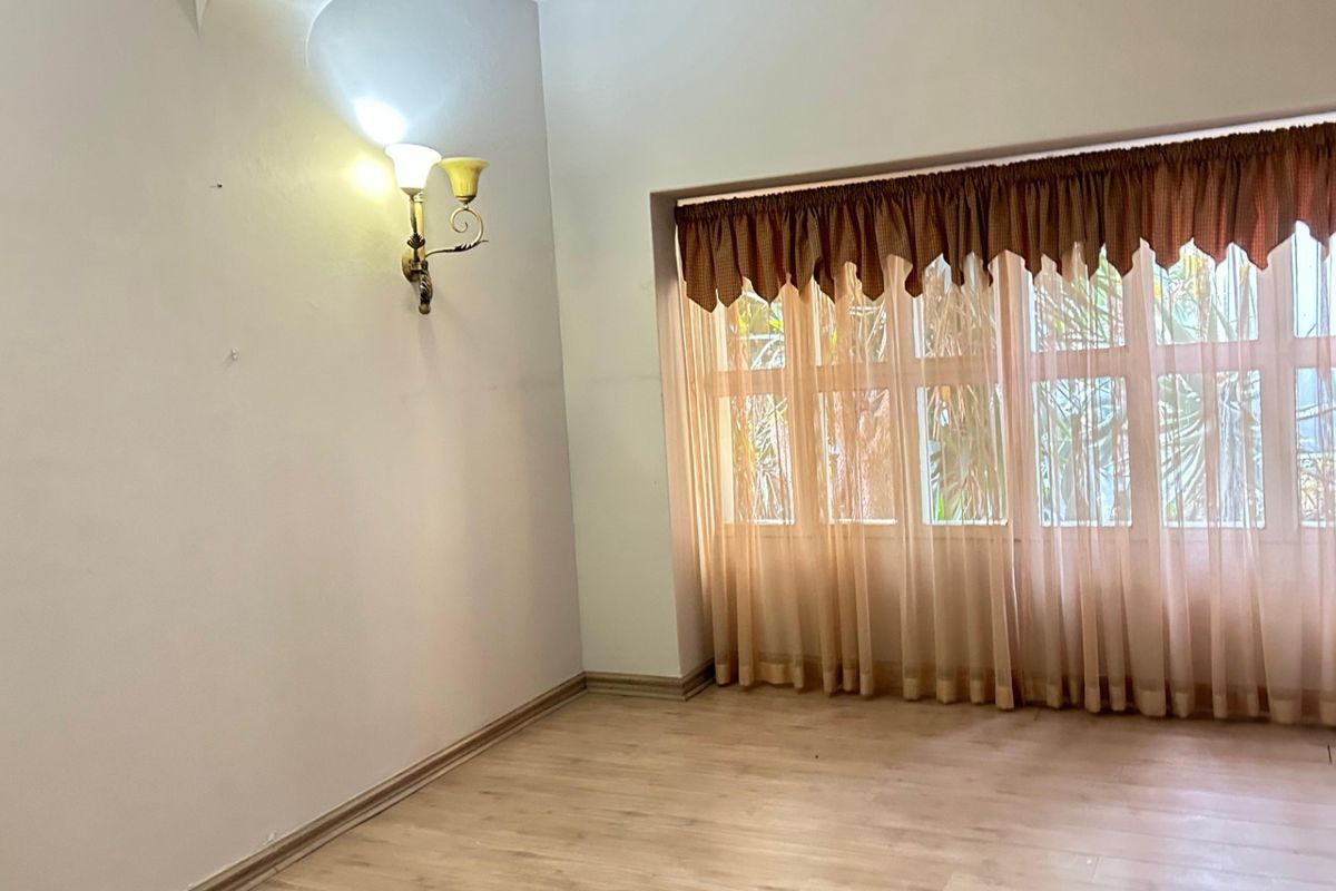A bright, empty living room featuring laminate flooring, a large window with curtains, and a wall-mounted light fixture.