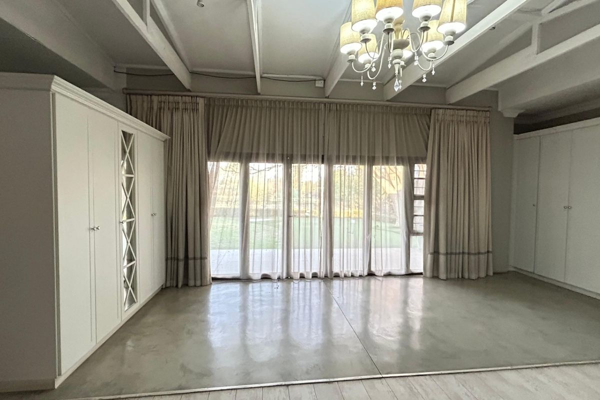 Spacious bedroom featuring polished concrete floors, exposed ceiling beams, extensive built-in cabinetry, and large sliding doors opening to the garden.