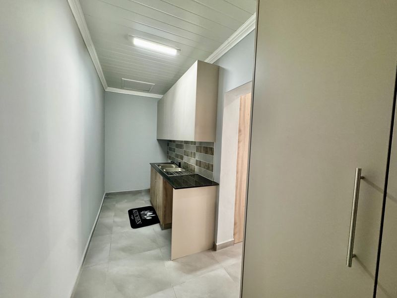 A clean and functional scullery area featuring built-in cabinetry, a stainless steel sink, and modern tiled backsplash, providing efficient additional prep space.