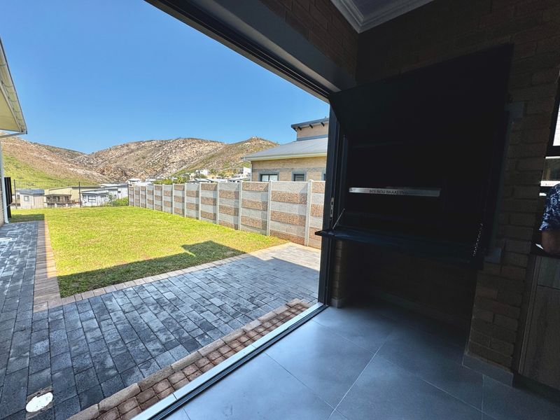 Covered patio area featuring a built-in braai, tiled flooring, and direct access to a paved outdoor space and garden with mountain views.
