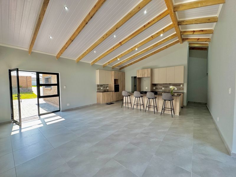 Spacious open-plan living and kitchen area featuring high vaulted ceilings with exposed timber beams, modern cabinetry, and large format floor tiles.