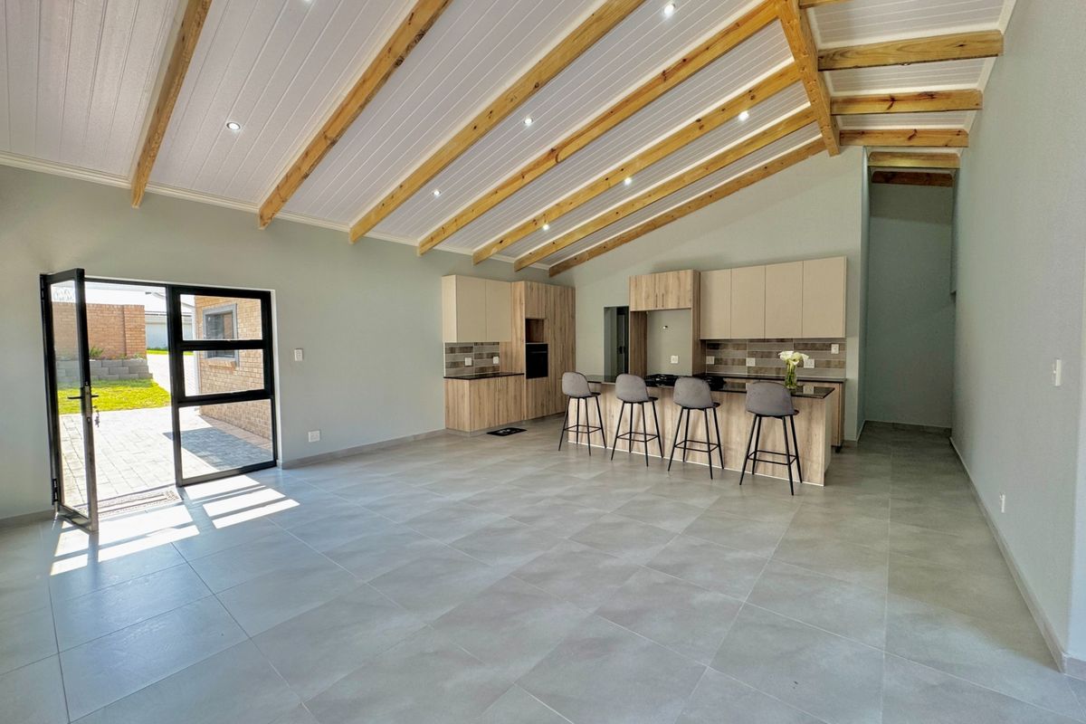 Spacious open-plan living and kitchen area featuring high vaulted ceilings with exposed timber beams, modern cabinetry, and large format floor tiles.