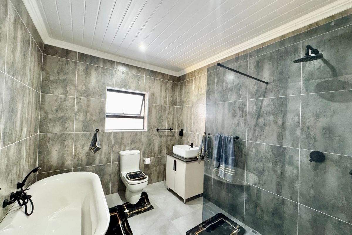Modern bathroom featuring a freestanding bathtub, a spacious walk-in shower with a glass screen, a vessel sink vanity, and contemporary grey tiling.