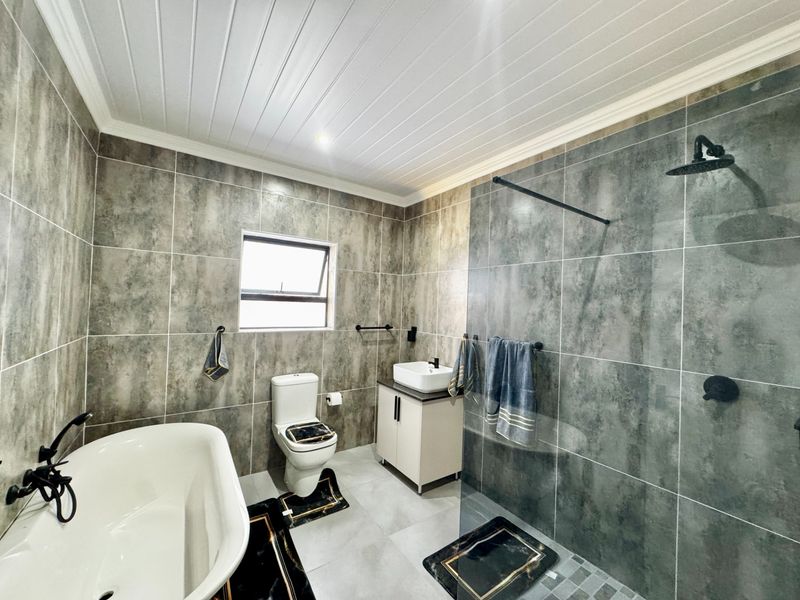 Modern bathroom featuring a freestanding bathtub, a spacious walk-in shower with a glass screen, a vessel sink vanity, and contemporary grey tiling.