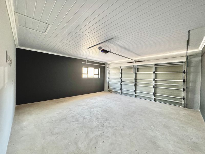 A clean, spacious, and well-maintained garage featuring a concrete floor, automated door mechanism, and a finished tongue and groove ceiling.