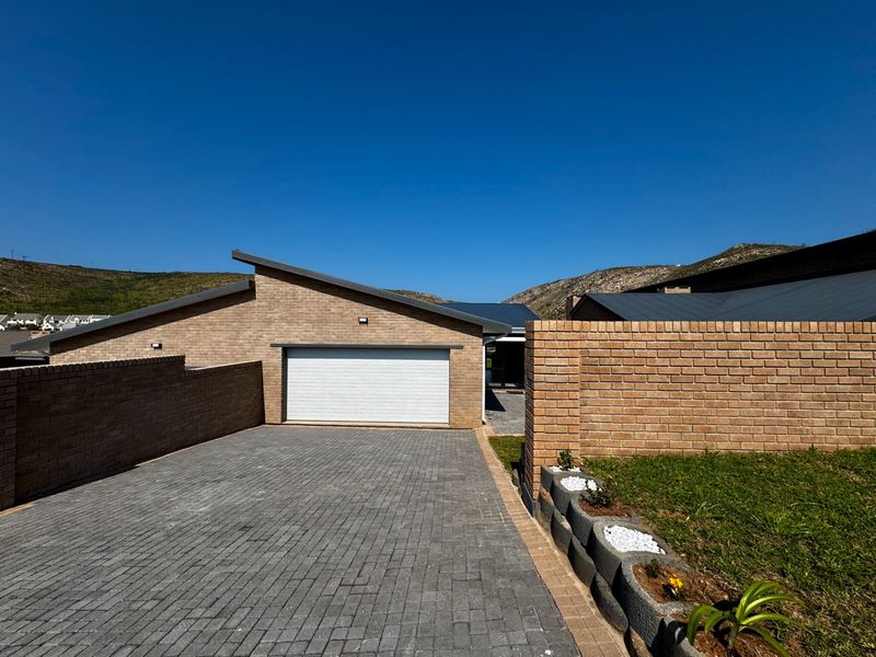 Front view of a modern brick house featuring a paved driveway, single garage door, and perimeter boundary wall.