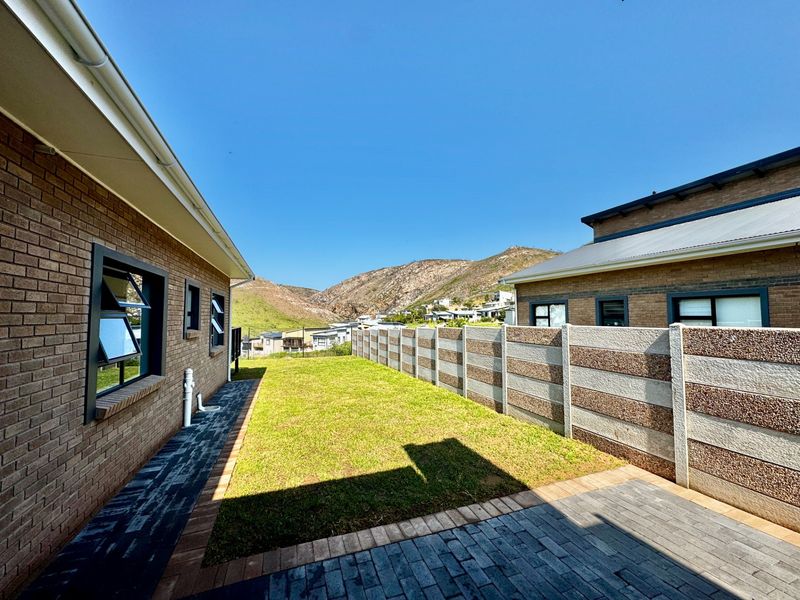 A well-maintained rear garden area featuring a paved walkway, lawn, and precast concrete boundary wall with mountain views in the background.