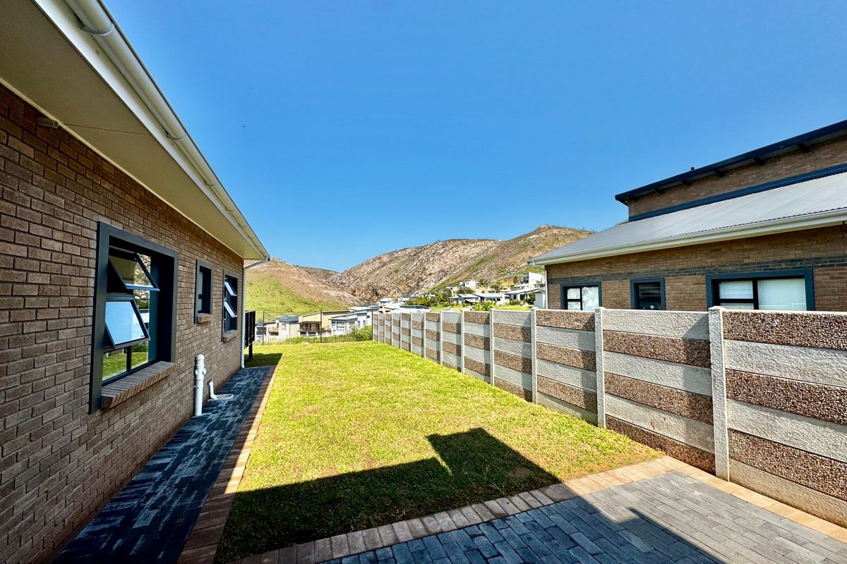 A well-maintained rear garden area featuring a paved walkway, lawn, and precast concrete boundary wall with mountain views in the background.