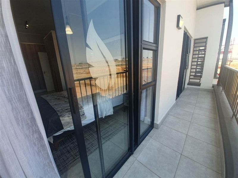 A modern balcony featuring tiled flooring, metal balustrades, and large sliding glass doors providing seamless access to the interior bedroom space.