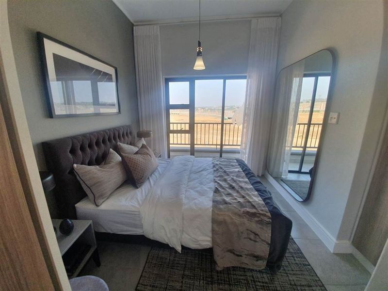 A modern bedroom featuring tiled flooring, a pendant light, and a large sliding glass door providing access to a balcony.