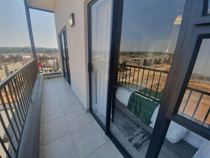 A modern apartment balcony featuring tiled flooring, a metal balustrade, and large sliding glass doors providing access to the interior living space.