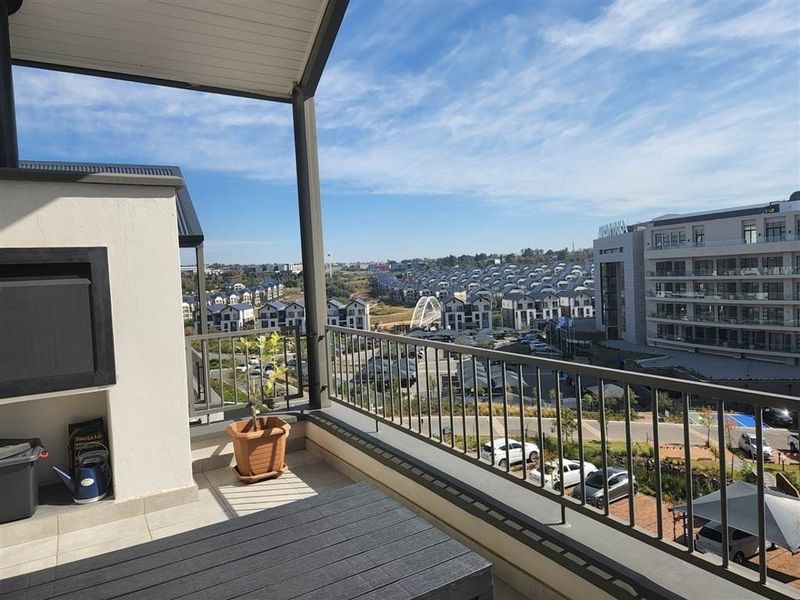 A spacious covered balcony featuring a built-in braai, metal balustrade, and expansive views of the surrounding residential estate.