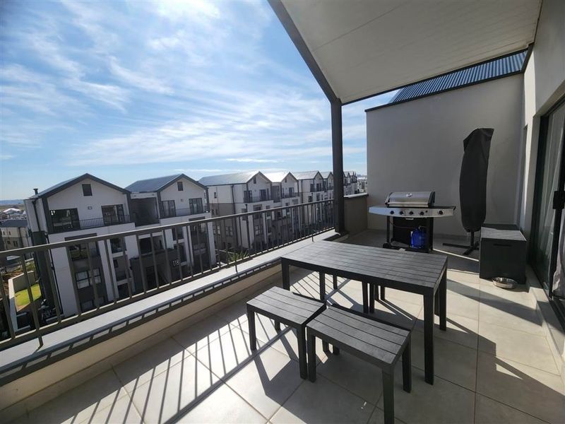 Spacious covered balcony featuring tiled flooring and a metal balustrade, offering an open outdoor area with views of the surrounding apartment complex.