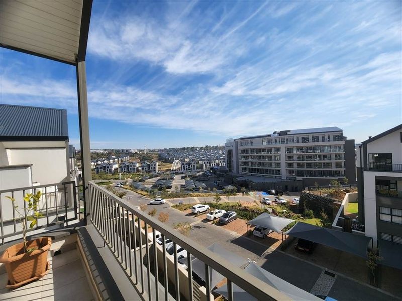 A modern balcony with metal balustrades and tiled flooring, offering an elevated view over the surrounding residential estate and parking area.