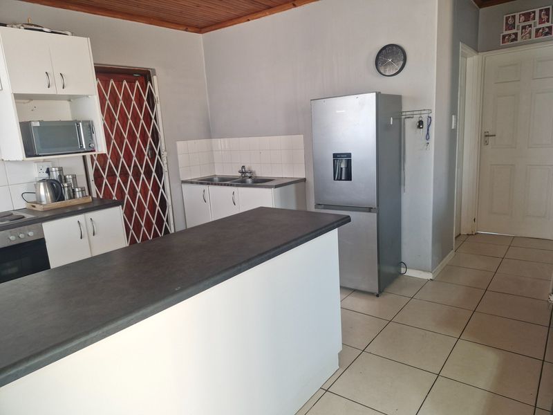 Functional kitchen featuring white cabinetry, dark laminate countertops, tiled backsplash, and ceramic flooring with a timber ceiling finish.