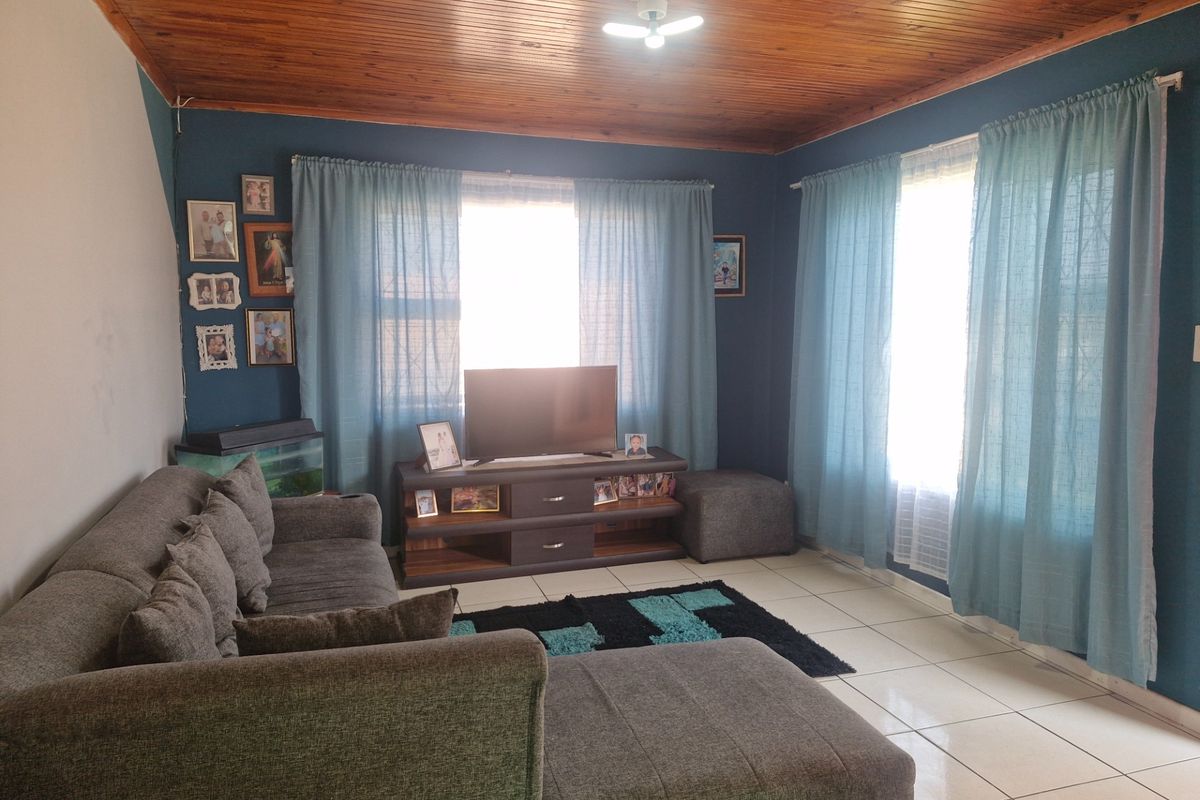 A living room featuring ceramic floor tiles and a timber tongue and groove ceiling, with natural light entering through windows fitted with security bars.