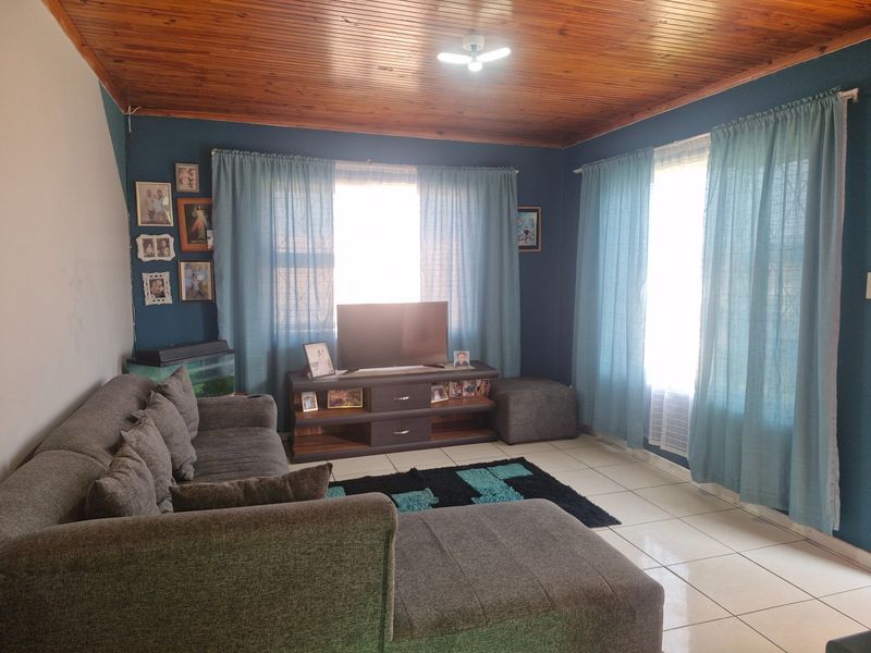 A living room featuring ceramic floor tiles and a timber tongue and groove ceiling, with natural light entering through windows fitted with security bars.