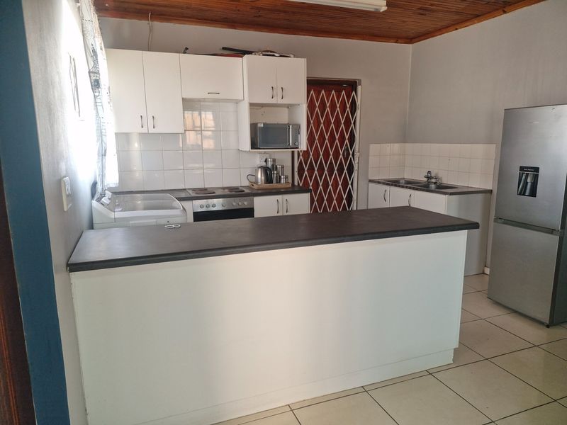 Functional kitchen featuring white cabinetry, laminate countertops, tiled backsplash, and a breakfast bar, complemented by a timber ceiling and tiled flooring.