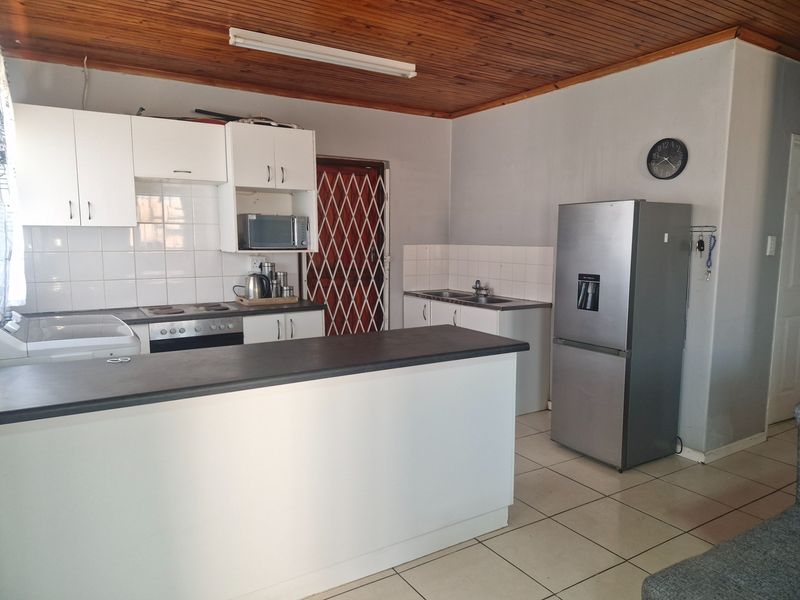 Open plan kitchen featuring white cabinetry, tiled splashbacks, electric hob, oven, and a breakfast bar, set under a timber-clad ceiling.