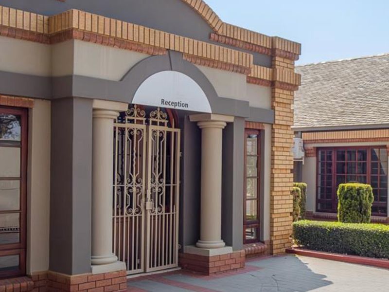 Front entrance facade featuring decorative columns, a secure wrought iron gate, and well-maintained brickwork with manicured landscaping.