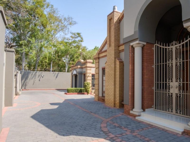 Front exterior view of the property featuring a paved driveway, brick facade, decorative columns, and a secure entrance gate.