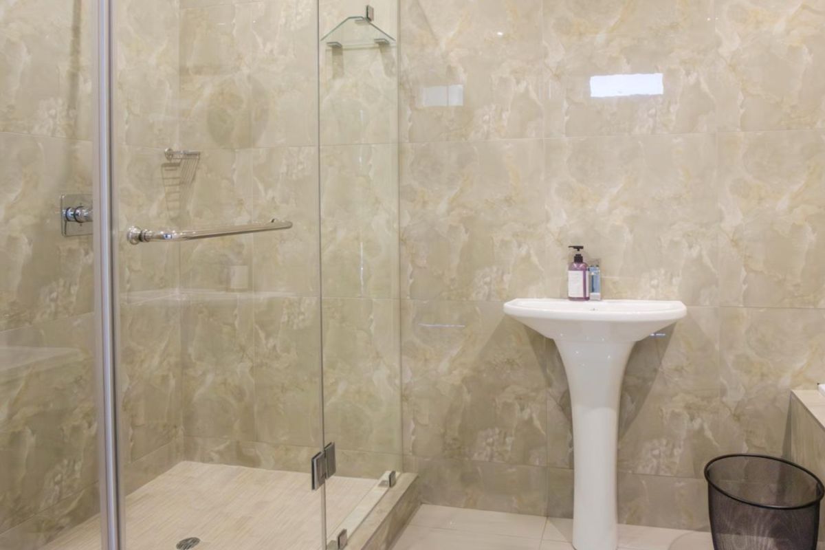 A modern bathroom featuring a pedestal basin and a glass-enclosed shower with neutral marble-look wall tiling.