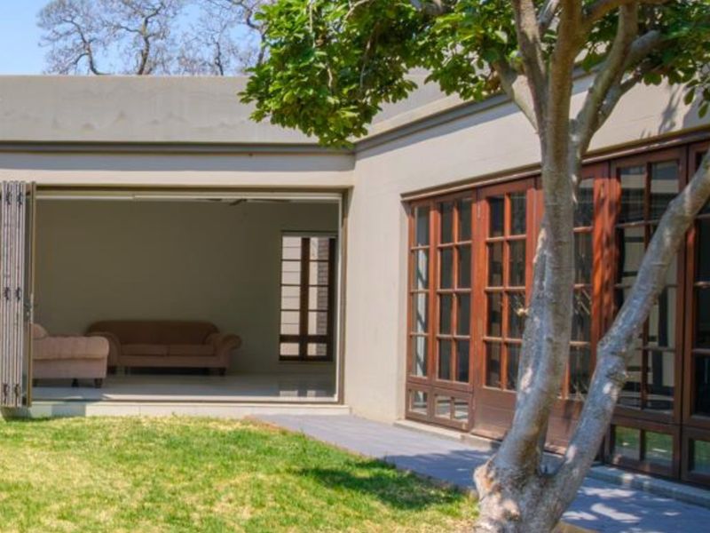 Rear view of the property featuring a landscaped garden, paved walkway, and large wooden-framed bi-fold doors leading into the living area.