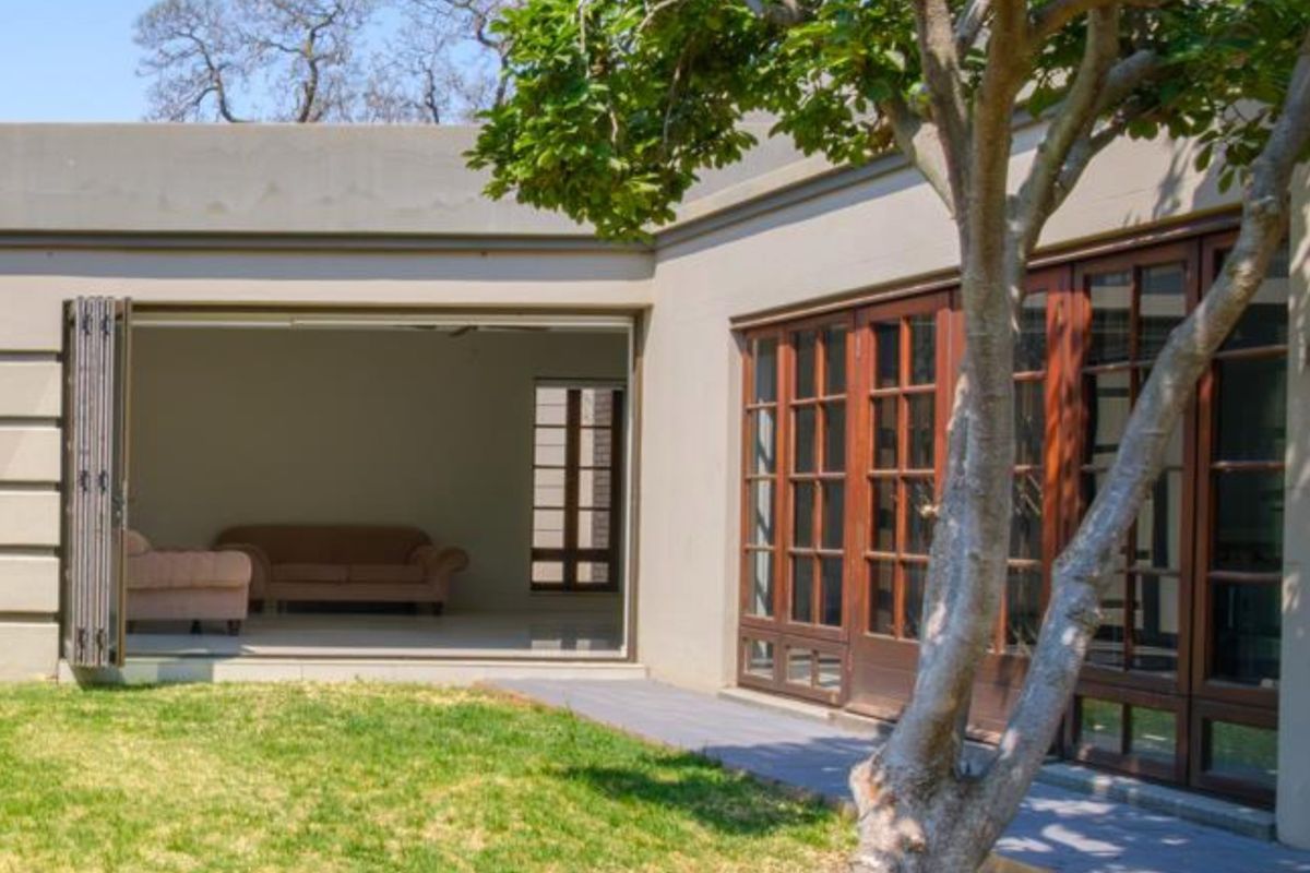 Rear view of the property featuring a landscaped garden, paved walkway, and large wooden-framed bi-fold doors leading into the living area.